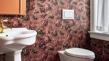 Ein Badezimmer mit blumigem Wandpapier, einem weißen Waschbecken und einer Toilette.