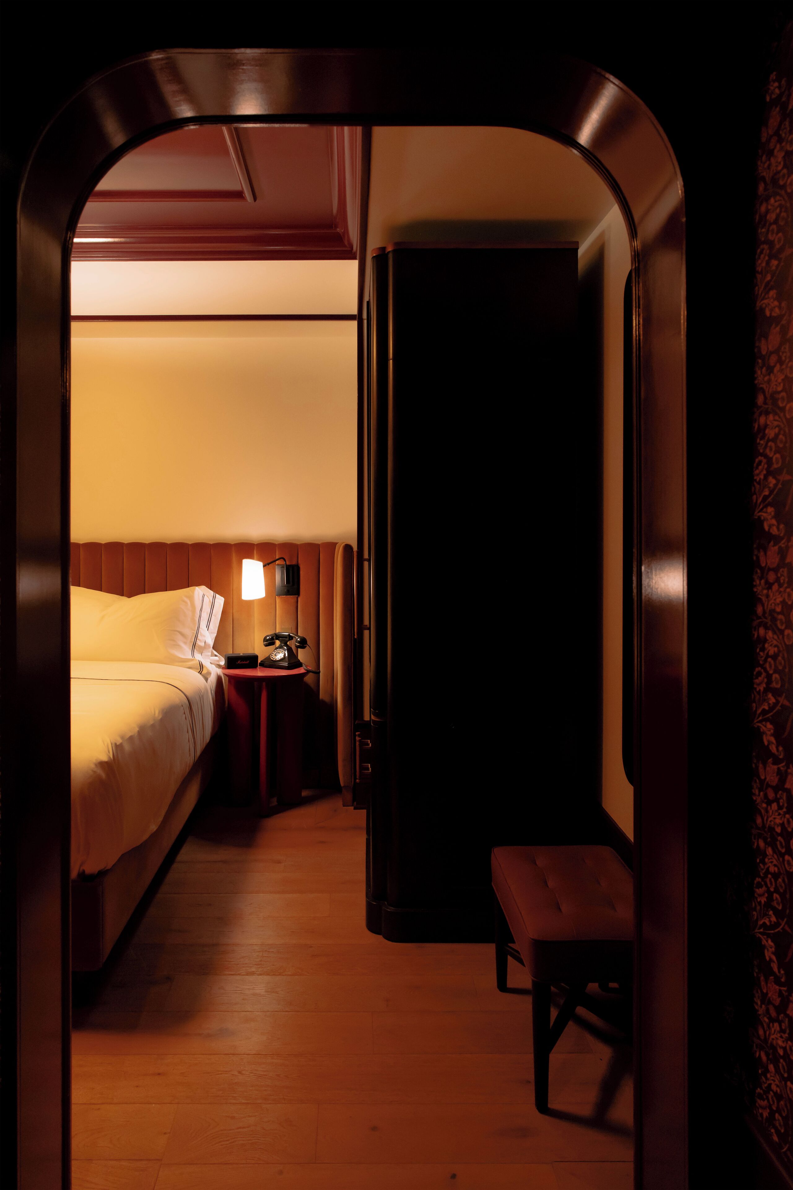 A hotel room with a bed, bedside table with a lamp, and a bench.