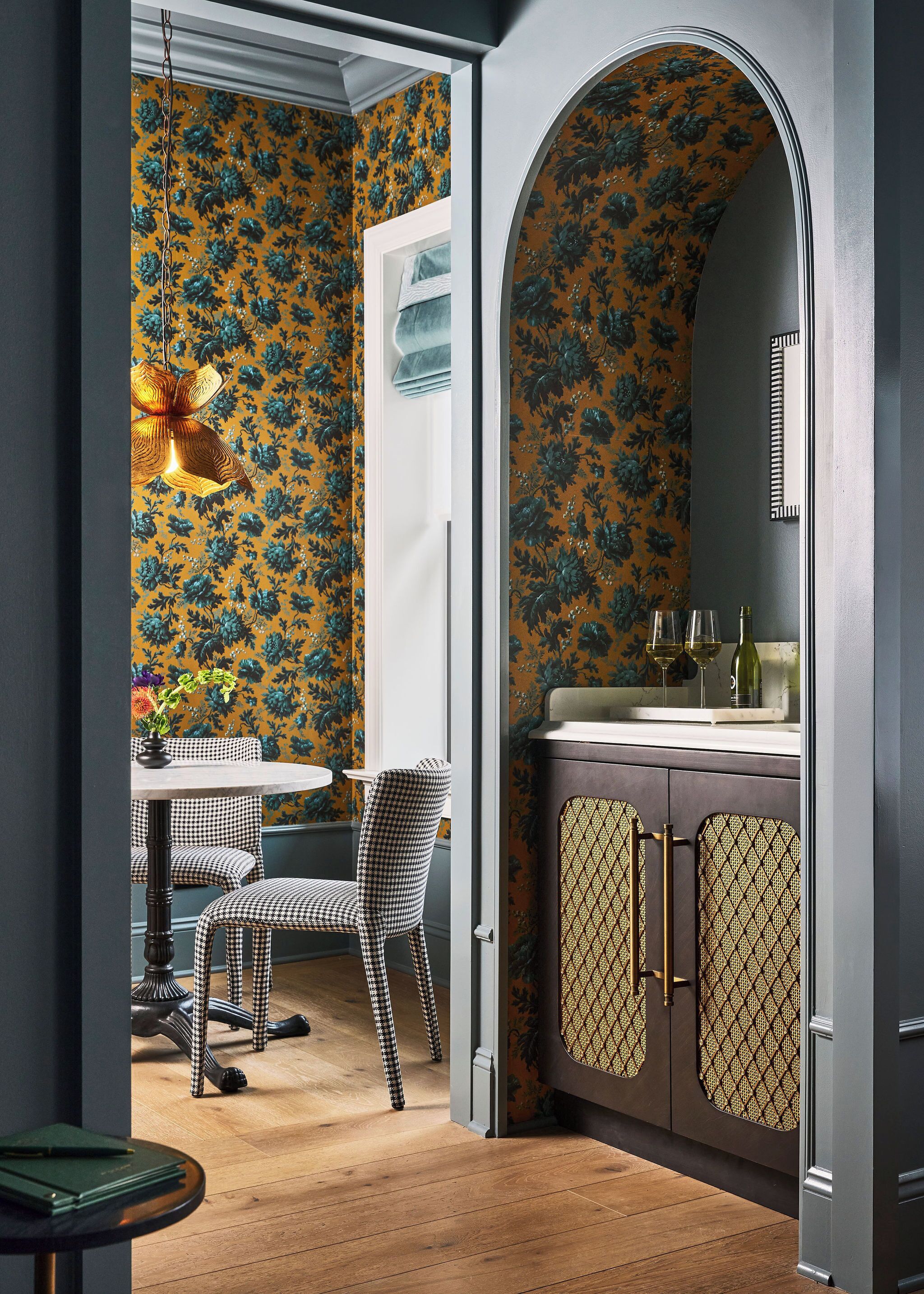 Ein Zimmer mit einem karierten Sessel, einem Tisch mit einer Vase und einem Schrank mit gemusterten Türen.