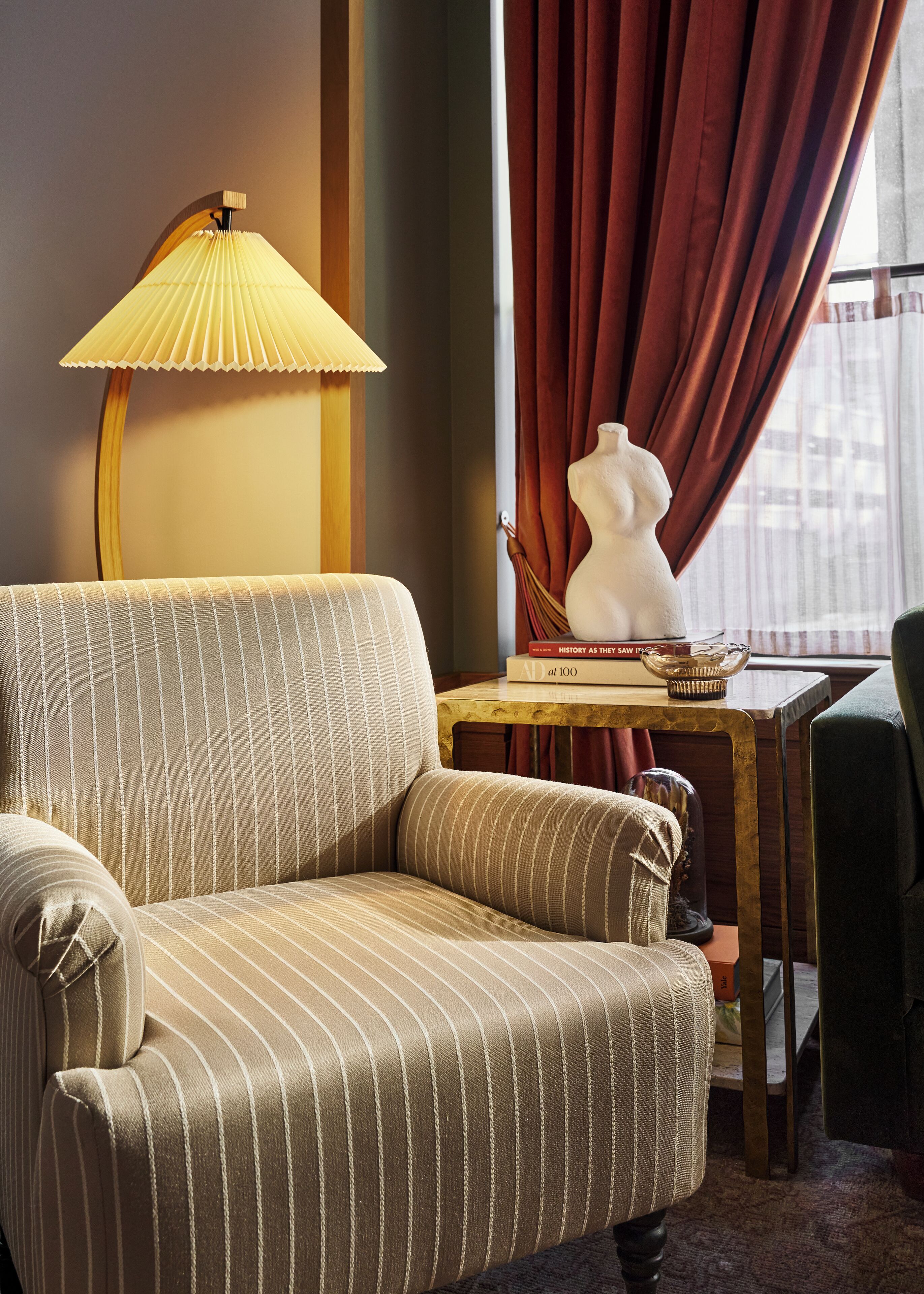 A striped armchair, a lamp, a mannequin bust, and a table with a book and a basket.