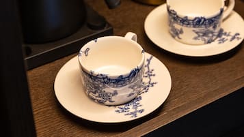 Une étagère en bois sur laquelle se trouvent une bouilloire électrique noire, une théière en laiton et deux tasses bleu et blanc à motifs, posées sur leurs soucoupes.