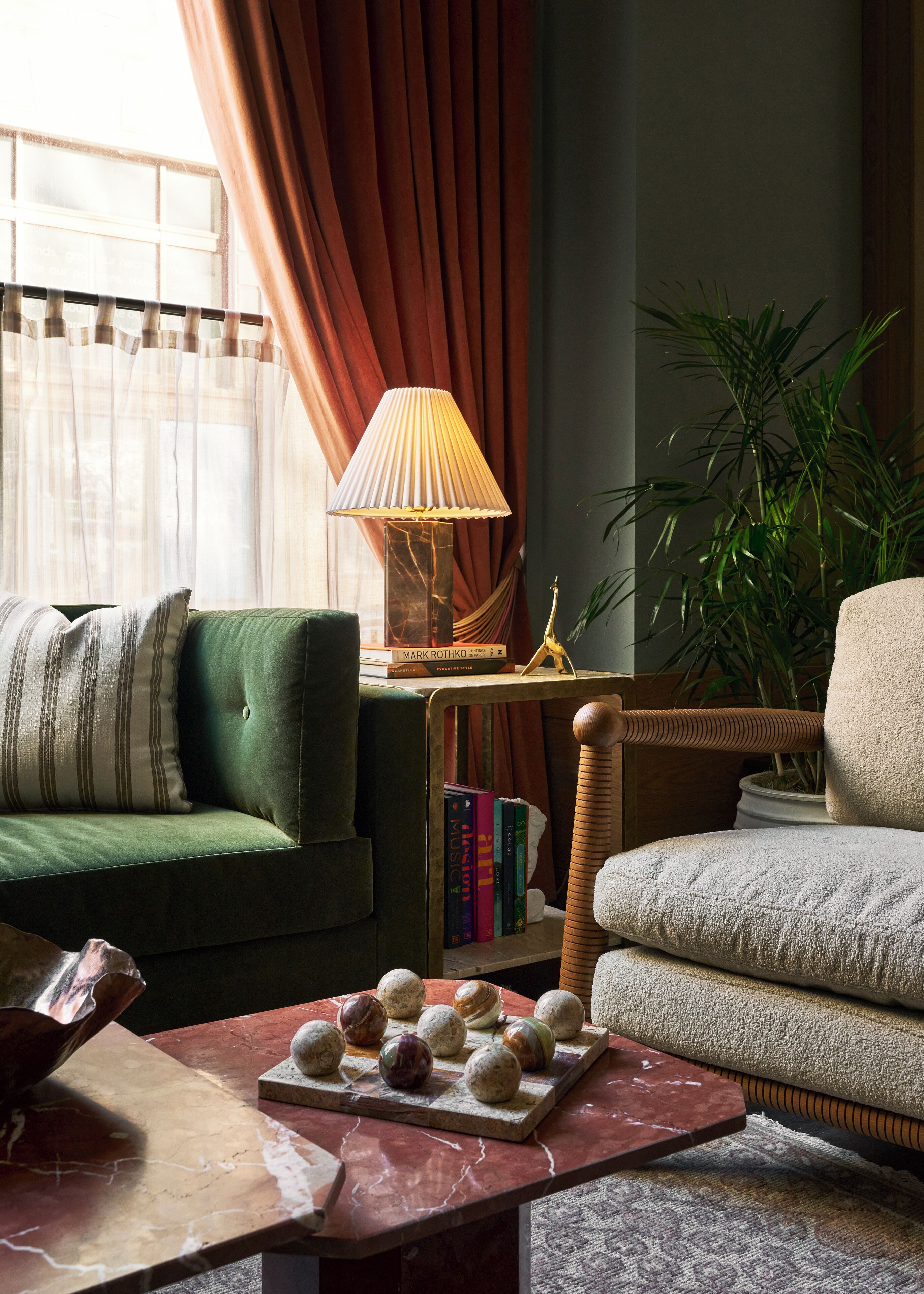 A cozy living room with a green sofa, a beige armchair, a wooden coffee table with decorative stones, a lamp, and a bookshelf.