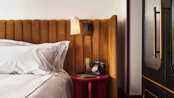 A neatly made bed with white linens, a red bedside table with a lamp, a telephone, and a green folder.
