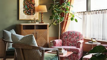 A cozy living room with a patterned armchair, a wooden side table, a floor lamp, and a large green plant.