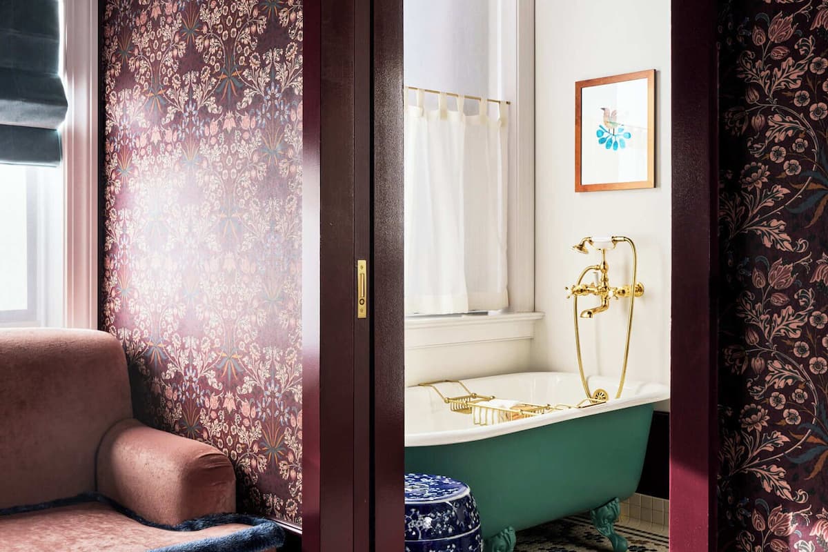 Una habitación con una bañera de patas de león antigua, un taburete de cerámica azul y un tapete estampado.