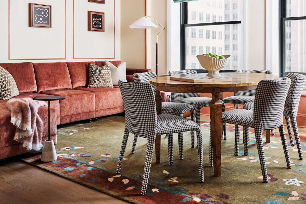 Un salón con un sofá rojo, sillas a cuadros, una mesa de madera y una araña.