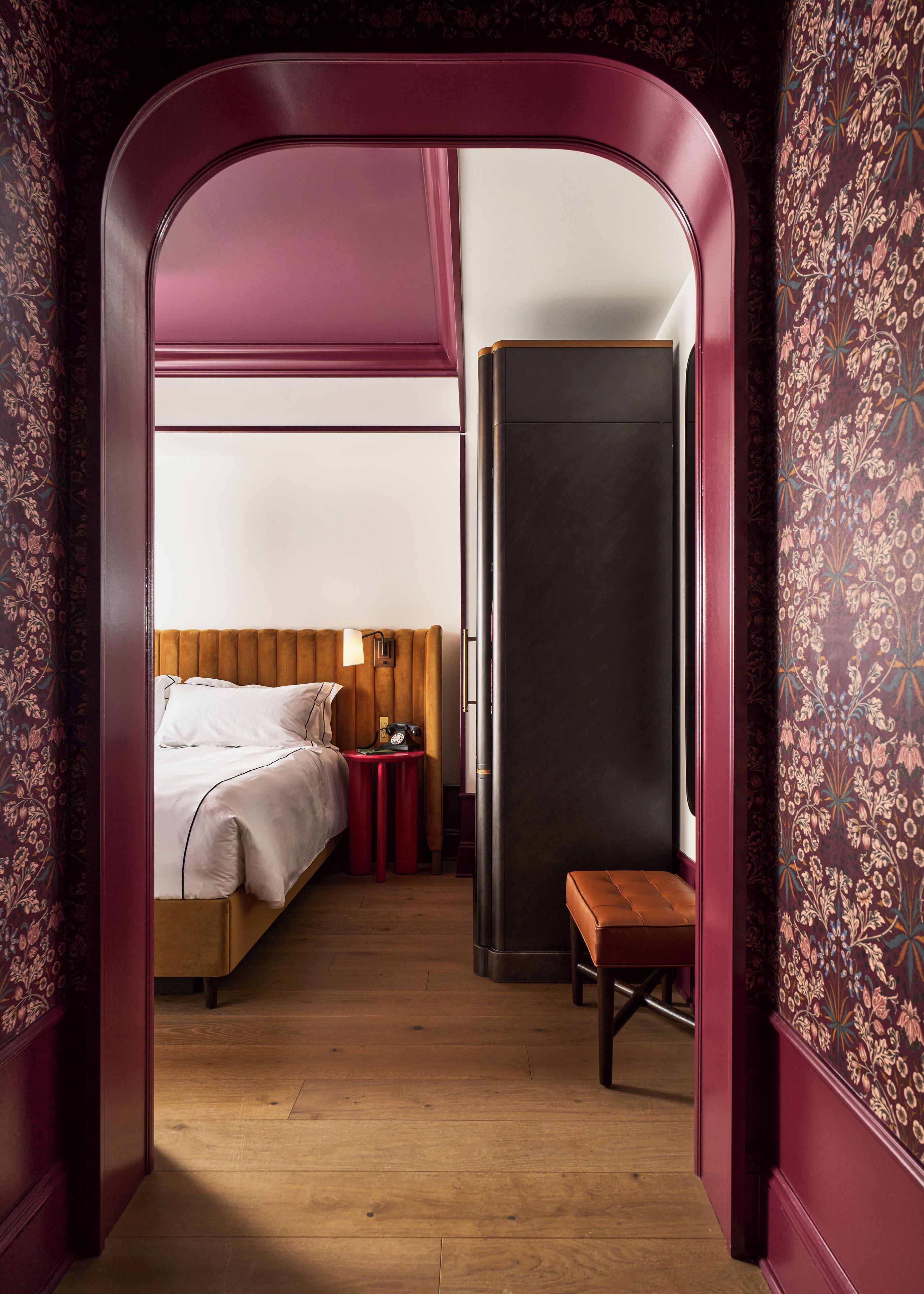 A bedroom with a bed, bedside table, lamp, and a bench.