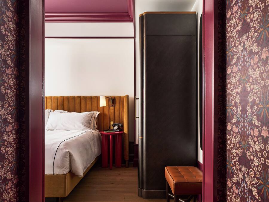 A bedroom with a bed, bedside table, lamp, and a bench.