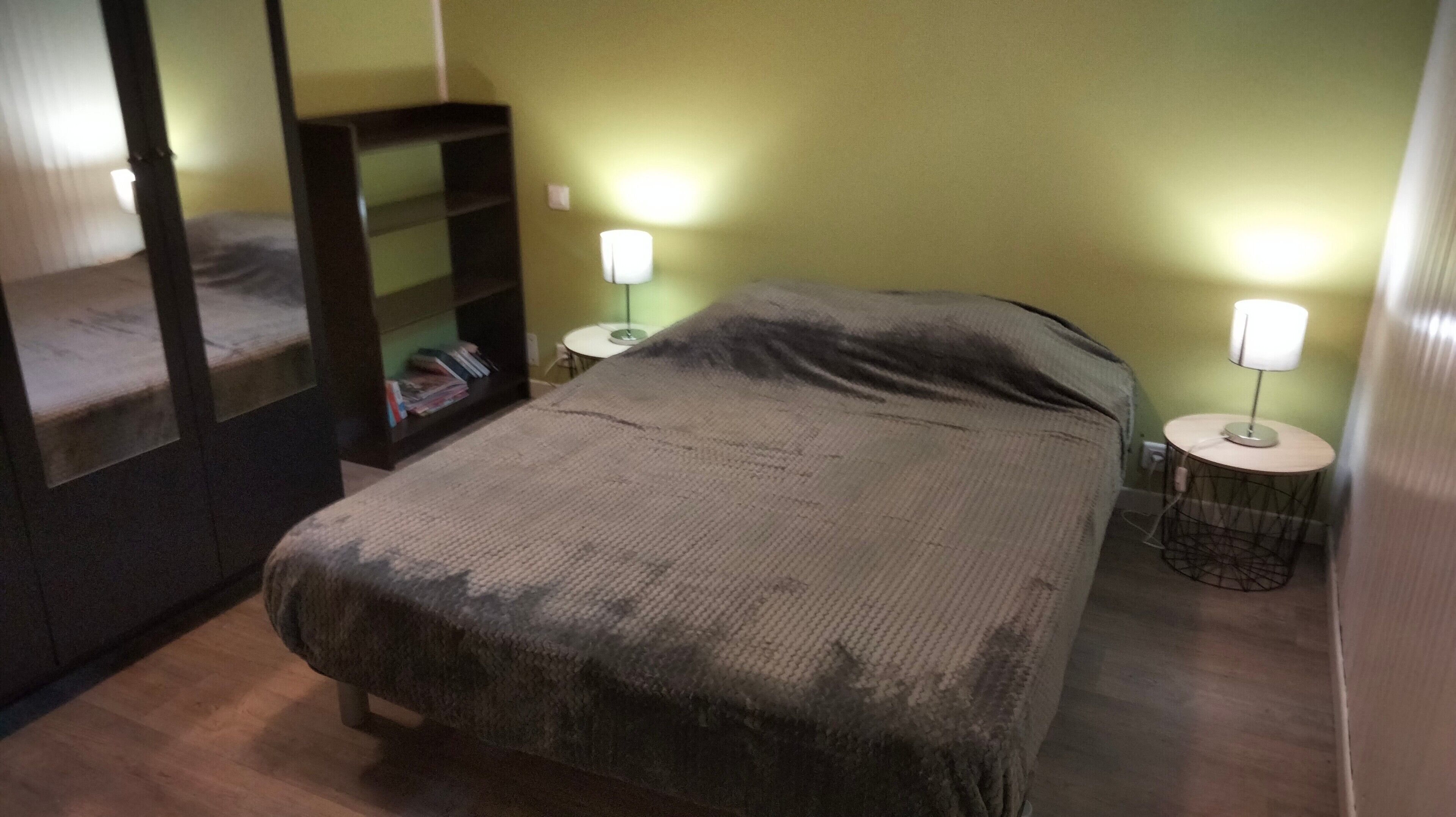 Et værelse med en seng, et natbord, en lampe, et spejl og en bogreol.