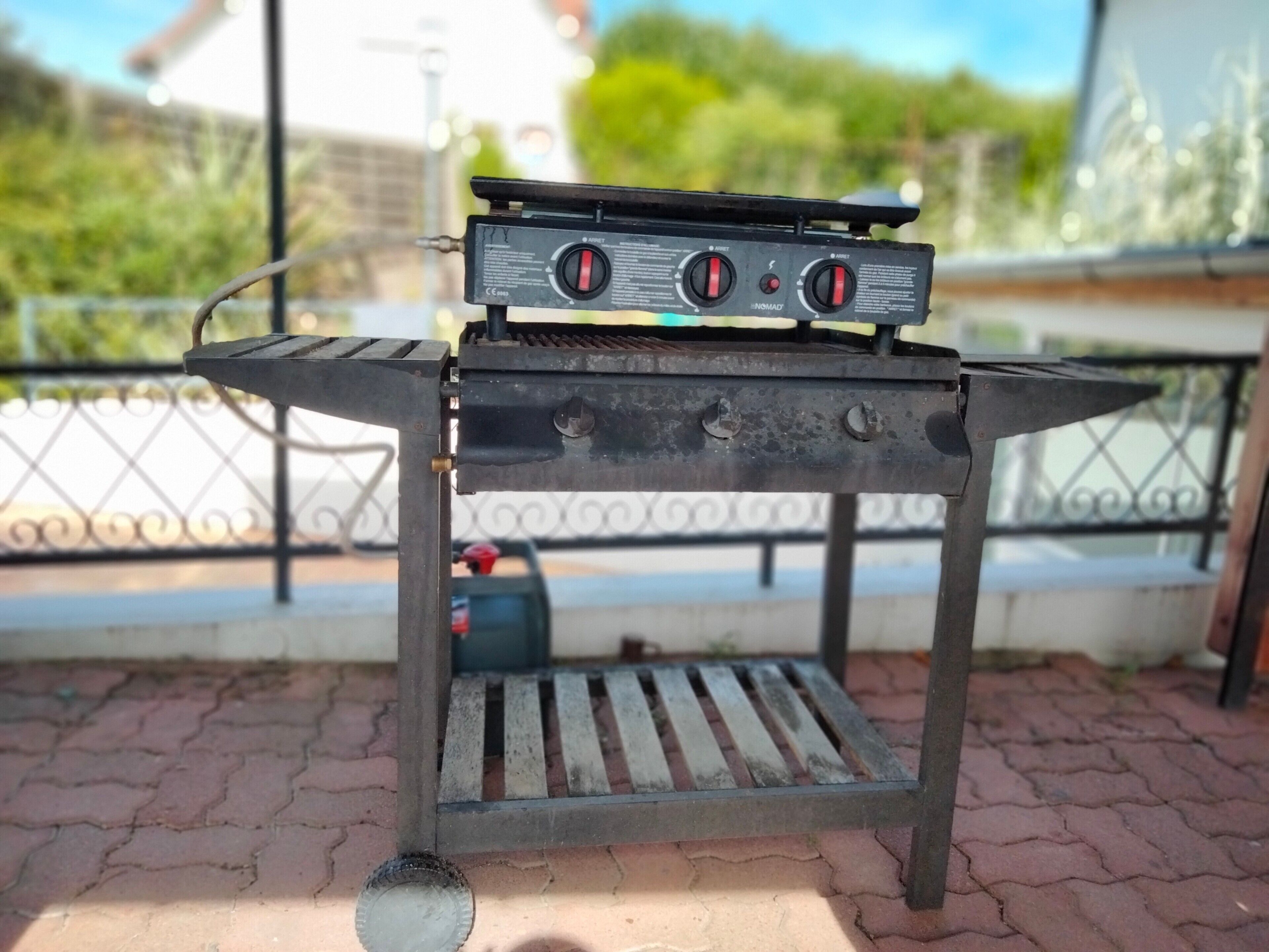 A portable gas grill with a control panel, placed on a metal stand with a slatted base.