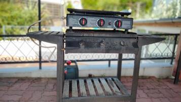 A portable gas grill with a control panel, placed on a metal stand with a slatted base.