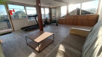A spacious living room with a treadmill, exercise bike, and a large window offering a view of the outdoors.