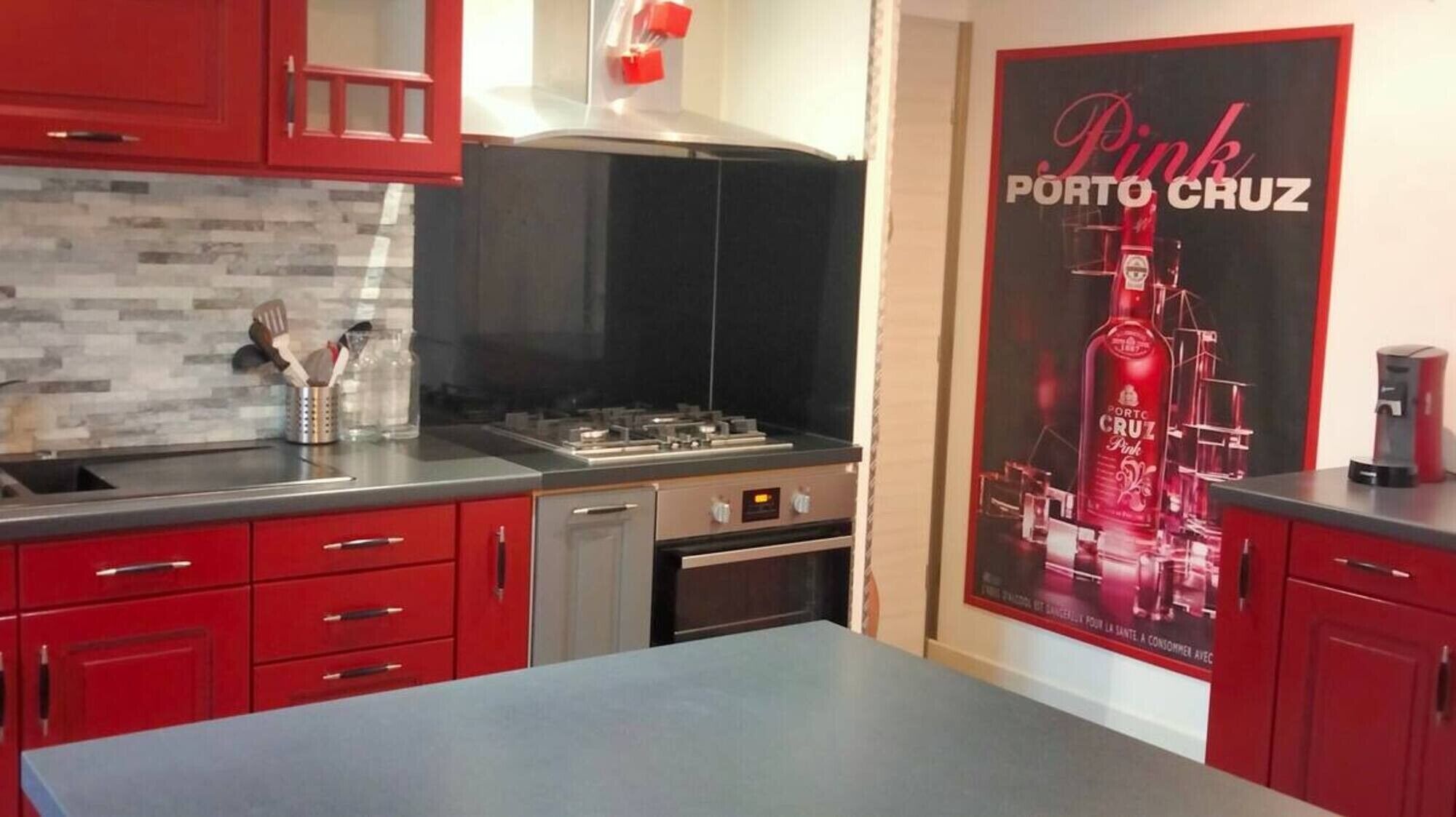 Een keuken met rode kastjes, een roestvrijstalen aanrecht, een gasfornuis en een koffieapparaat.