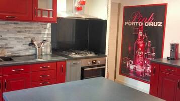 Een keuken met rode kastjes, een roestvrijstalen aanrecht, een gasfornuis en een koffieapparaat.