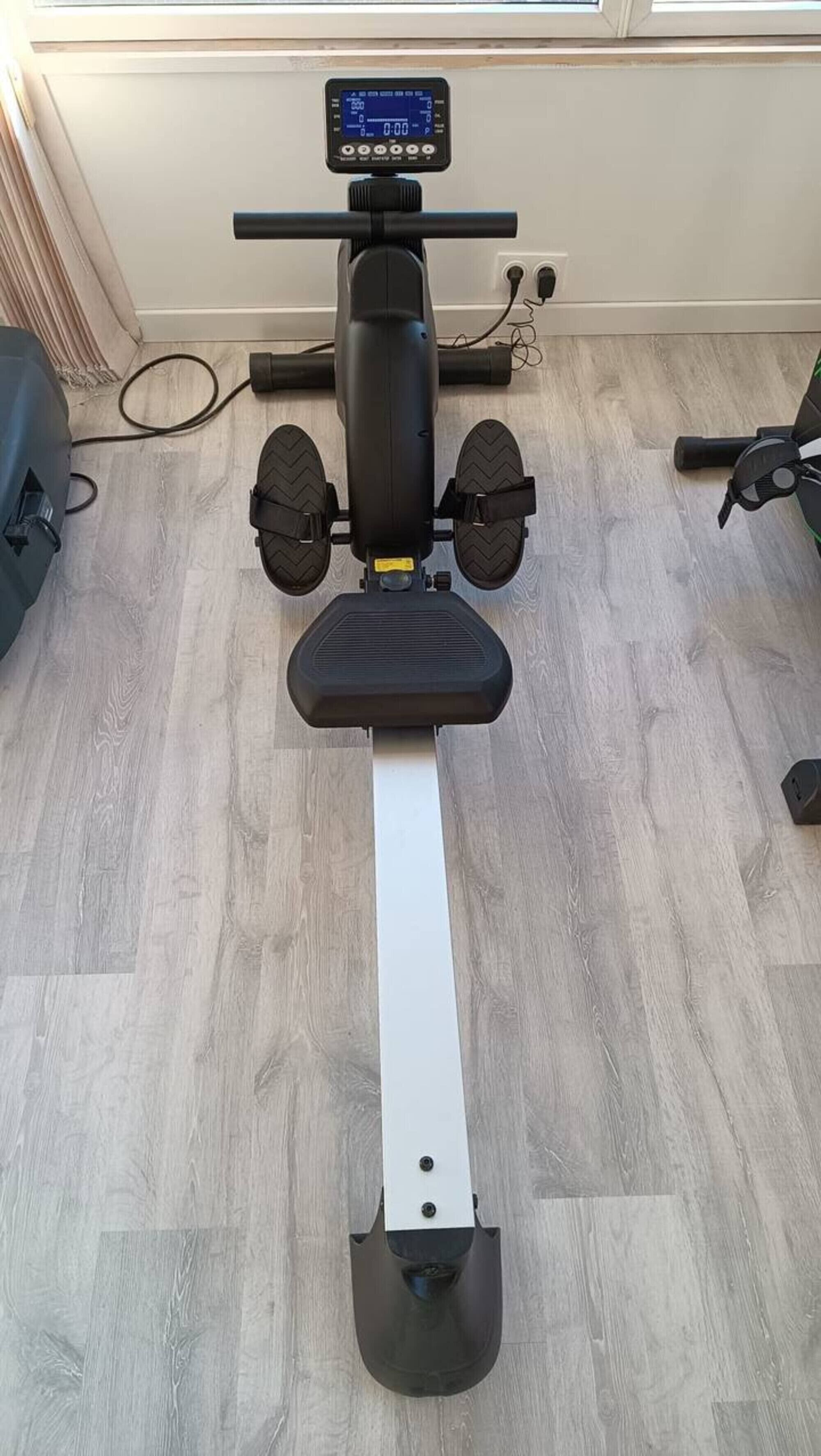 A stationary exercise bike with a digital display, a white seat, and a black footrest.