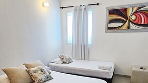 A room with two beds, a window with curtains, a wall-mounted light, and a colorful abstract painting. - PARCEROS GROUP - 2 BEDROOM VACATION APARTMENT, 6TH FLOOR, CARTAGENA, SPAIN (Cartagena de Indias)