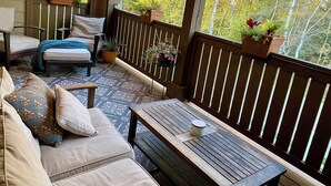Un espace extérieur abrité, doté d’une table en bois, de sièges rembourrés et de plantes en pot.