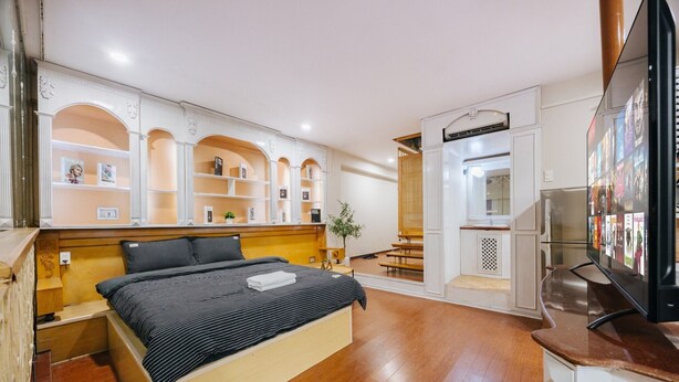 A modern bedroom with a wooden bed, built-in shelving, a TV, and a small seating area.