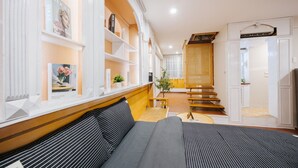 A modern hotel room with a large bed, a wooden staircase, and a bookshelf with magazines.