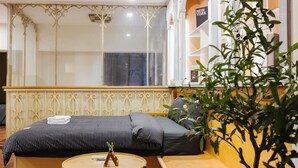 A hotel room with a bed, a round wooden table, a potted plant, and a view of the outside.