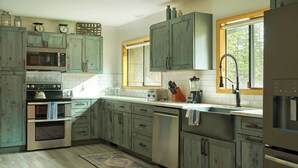 A kitchen with wooden cabinets, a microwave, oven, dishwasher, and a window with a view of trees. - Black Bear Lodge - Alpine Falls Ranch (Superior)