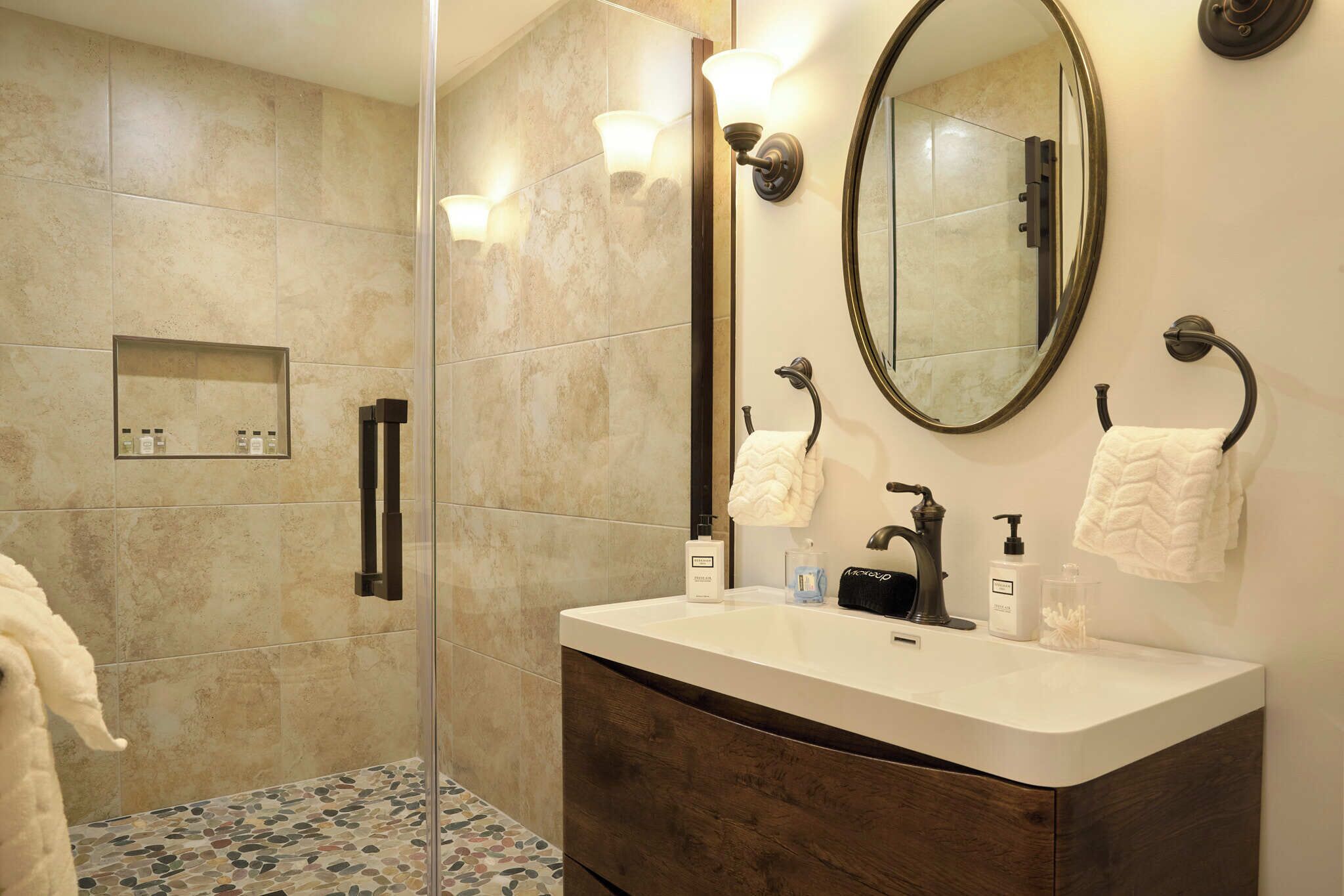 A modern bathroom with a glass-enclosed shower, a vanity with a dark wood cabinet, a large mirror, and a wall-mounted towel rack.