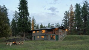 A two-story cabin with a balcony, surrounded by trees and a grassy area. - Black Bear Lodge - Alpine Falls Ranch (Superior)