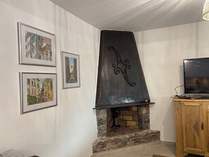 Un salon avec une cheminée en pierre, un téléviseur posé sur un meuble en bois et trois tableaux encadrés accrochés au mur.