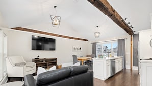 Eine moderne Küche mit weißen Schränken, ein Essbereich mit Holztisch und -stühlen sowie ein Wohnbereich mit einer schwarzen Ledersofa.