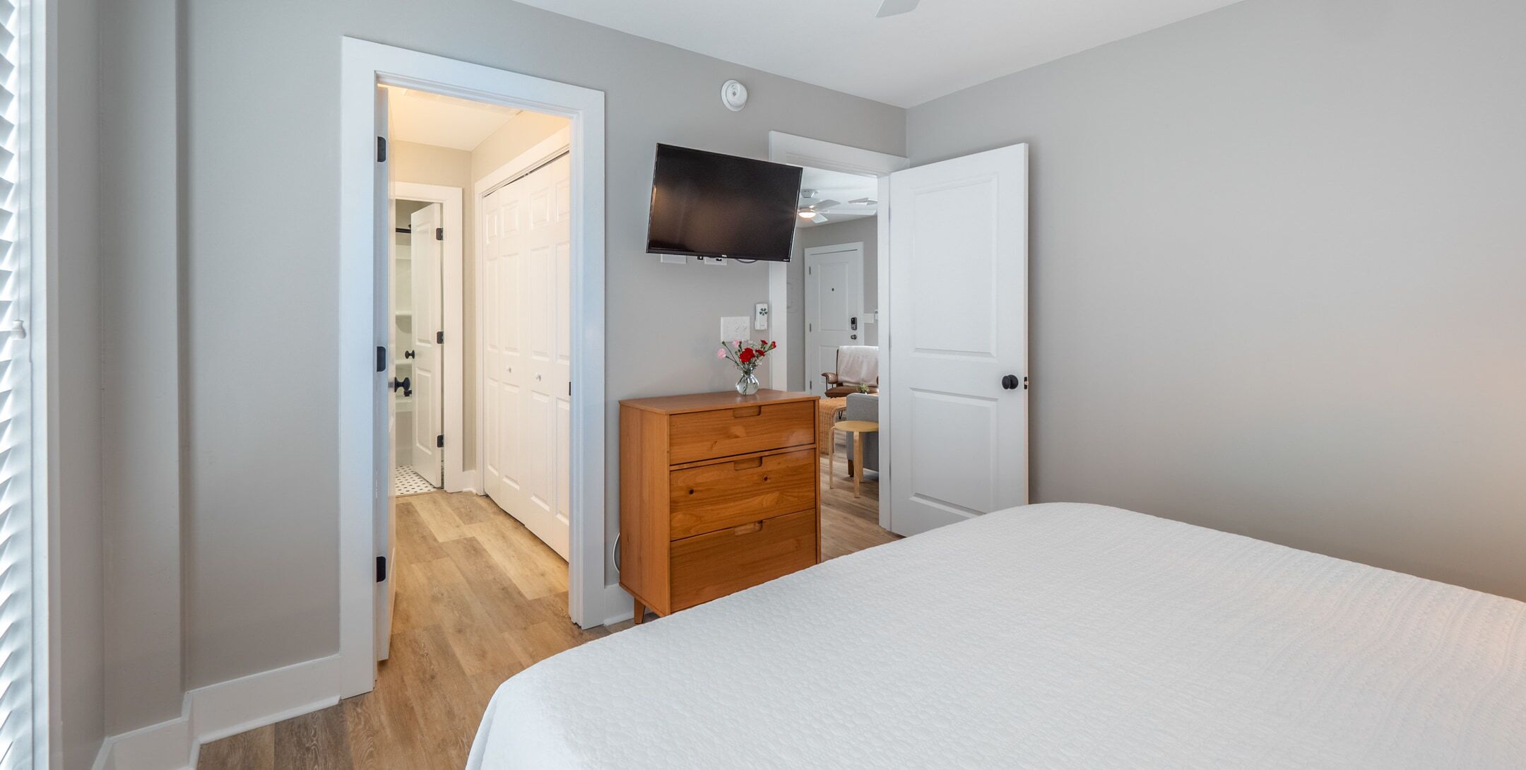 Un dormitorio con cama, cómoda, televisor y puerta que da a otra habitación.