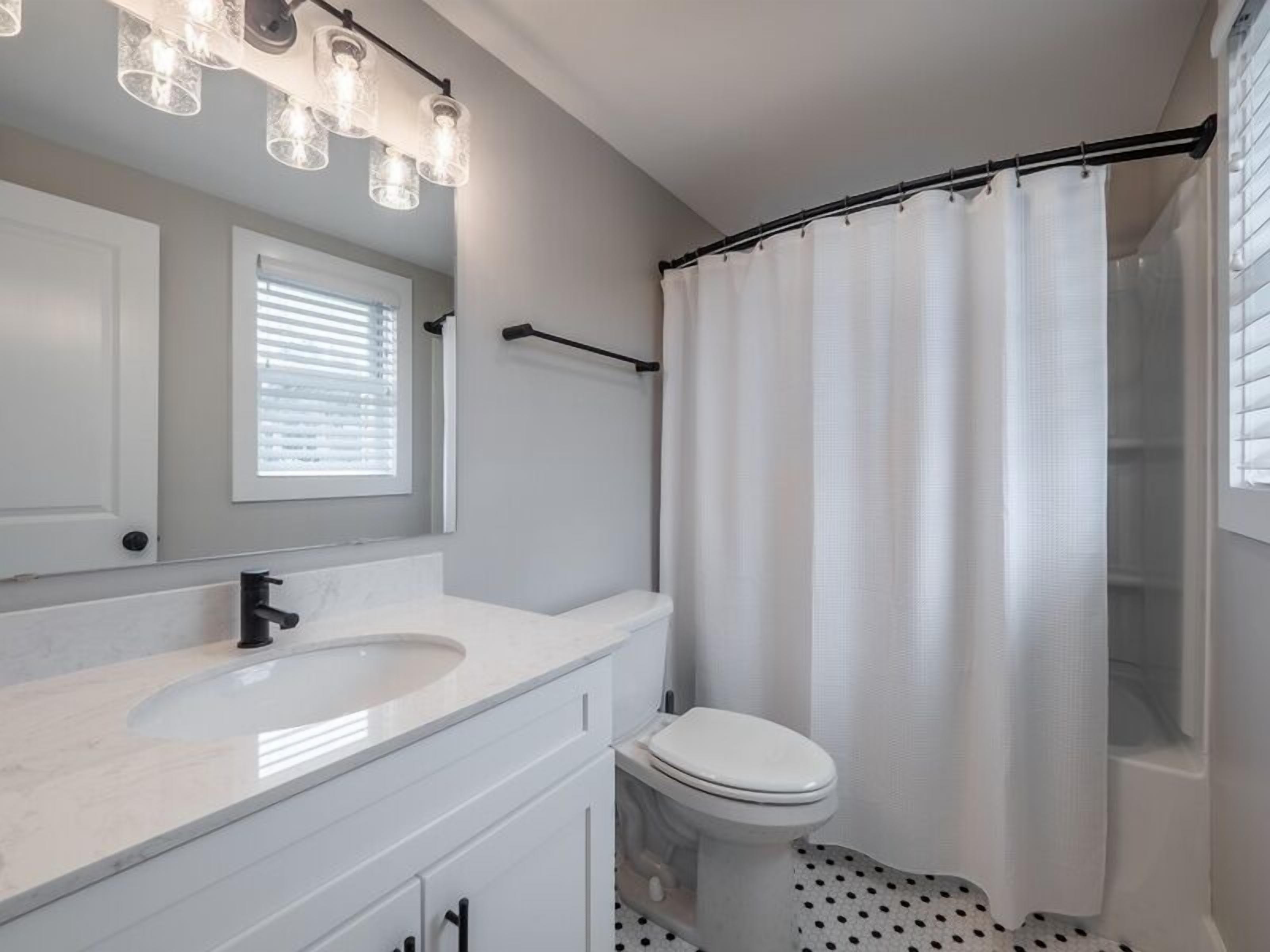 Un baño con lavamanos, inodoro y cortina de ducha blancos.