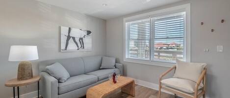 A modern living room with a grey sofa, a wooden coffee table, a wicker side table, a floor lamp, and a ceiling fan.