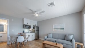 Un salon moderne avec un canapé gris, une table basse en bois et un coin repas comprenant des chaises blanches et une petite table.
