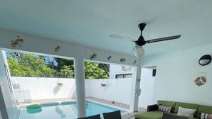 A poolside area with a table and chairs, a green sofa, and a ceiling fan. - villa ji (Las Terrenas)