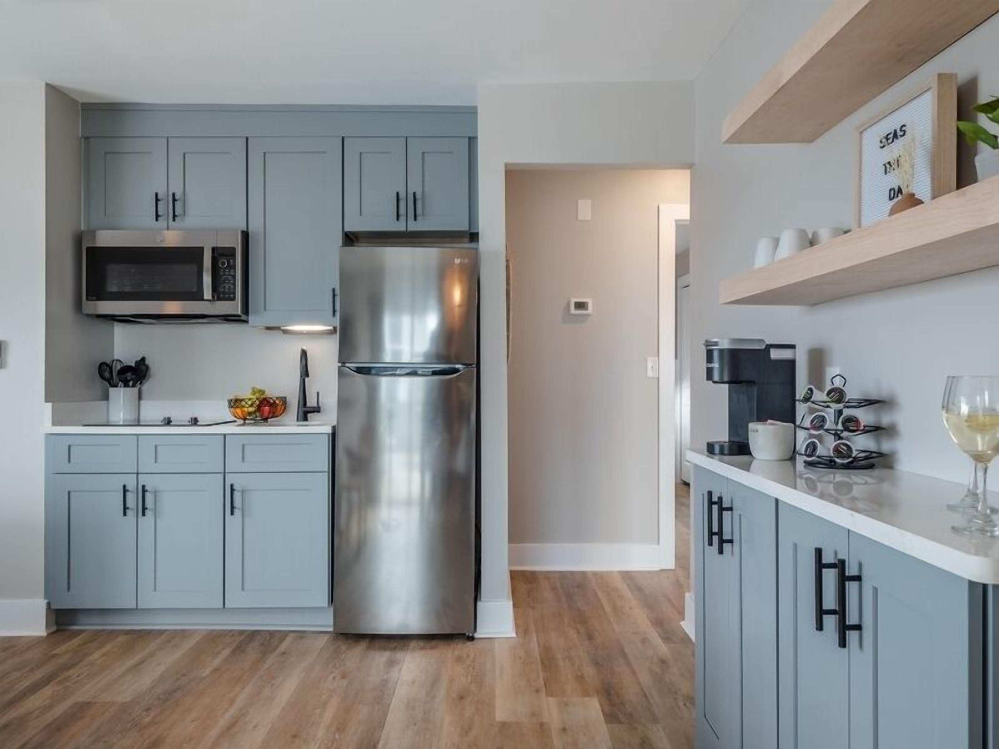 Una cocina moderna con armarios grises, un refrigerador de acero inoxidable, un microondas y una cafetera.