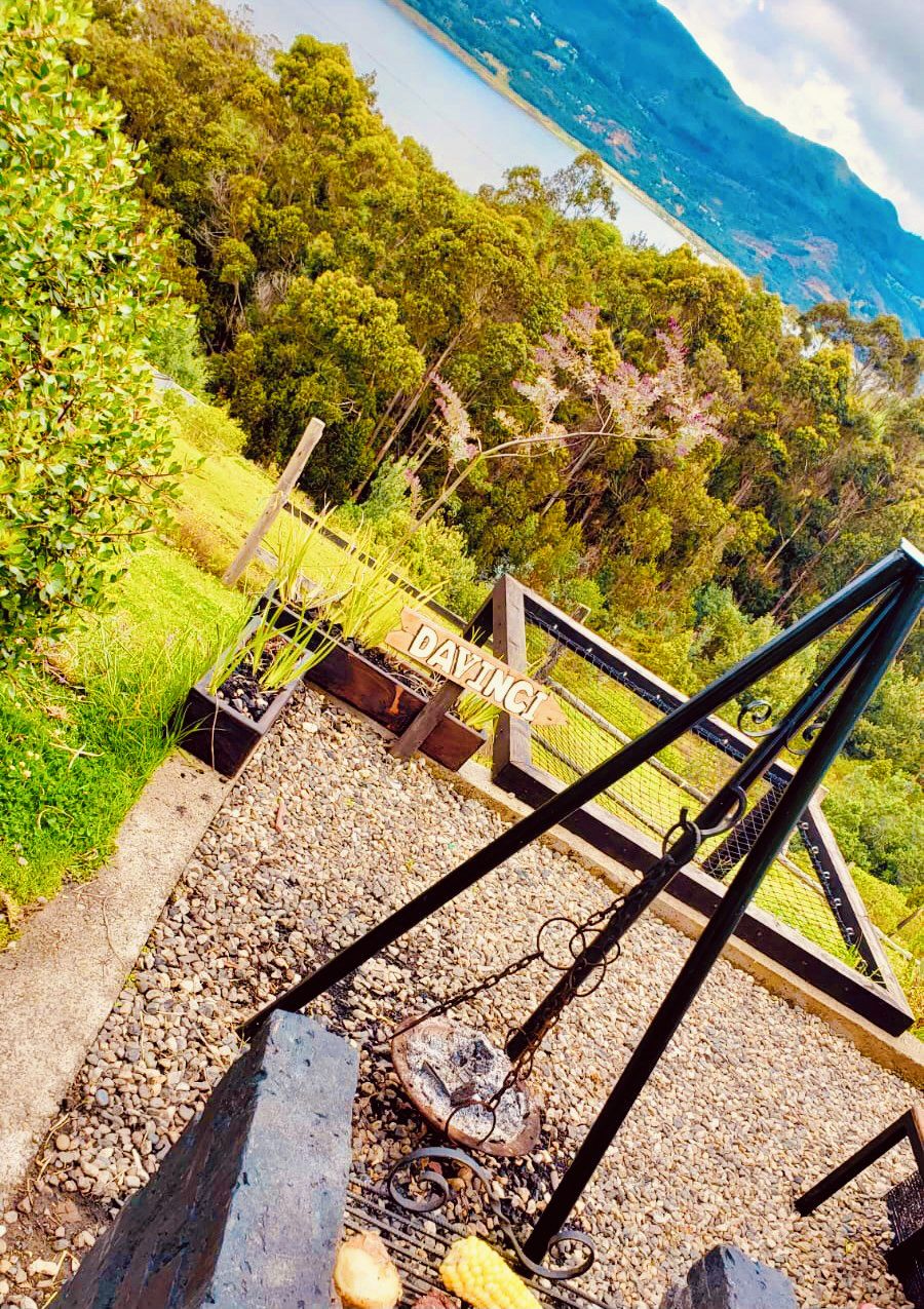 A rustic outdoor grill area with a wooden sign, surrounded by lush greenery and a mountainous backdrop.