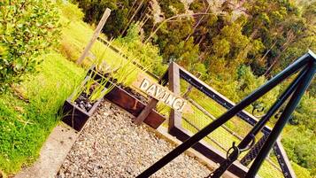 A rustic outdoor grill area with a wooden sign, surrounded by lush greenery and a mountainous backdrop.