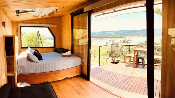 Een houten hutje met een bed, een tafeltje en uitzicht op een meer en bergen.