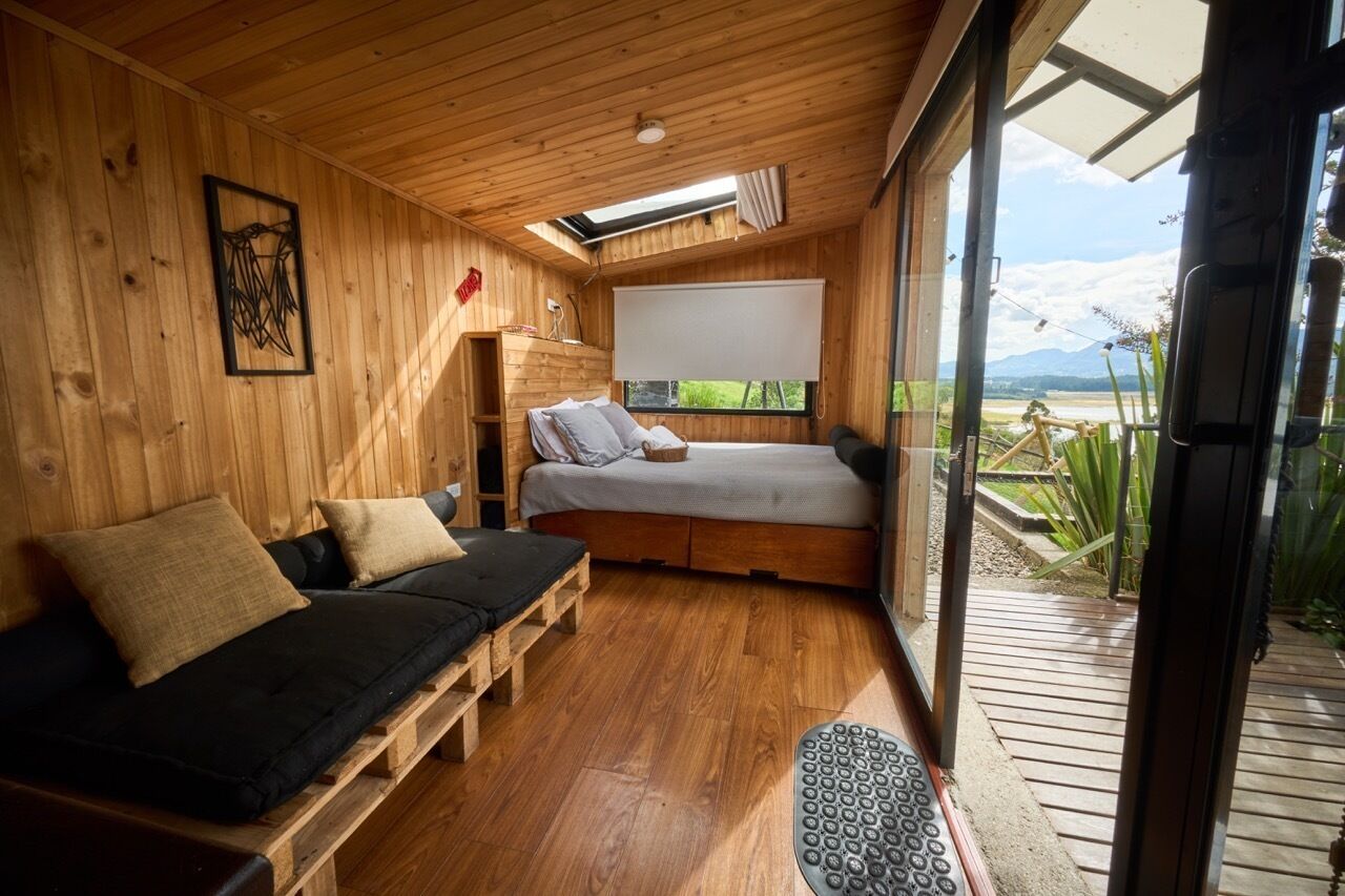 Interior d'una cabana de fusta amb un llit, un sofà i una finestra gran que ofereix vistes a l'exterior.