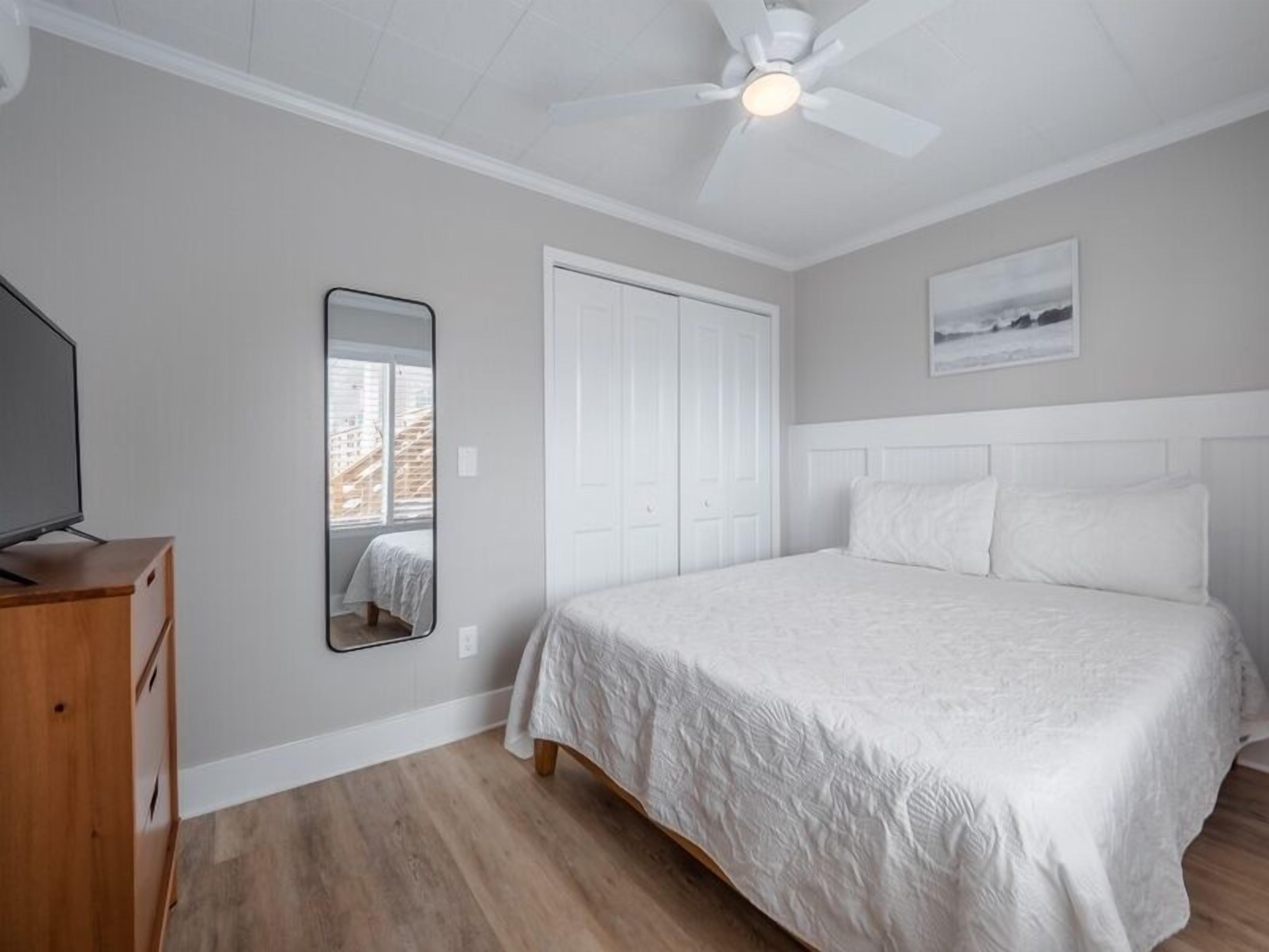 A bedroom with a bed, a ceiling fan, a dresser, and a window with a view of buildings.