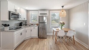 A modern kitchen with white cabinets, stainless steel appliances, and a dining area with a table and chairs. - Beach House OKI - Queen Suite in hotel on Oak Island, North Carolina (Oak Island)
