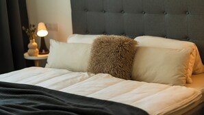 A neatly made bed with a tufted headboard, a bedside lamp, and a vase with flowers on a nightstand. - ALP DELUXE - Family-friendly and quiet vacation apartment with sauna & terrace (Weißenhorn)