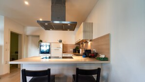 A modern kitchen with a large island, two black chairs, and a stainless steel range hood. - ALP DELUXE - Family-friendly and quiet vacation apartment with sauna & terrace (Weißenhorn)