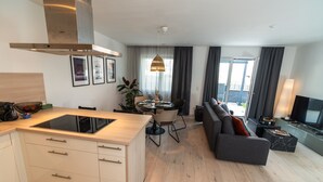 A modern kitchen with a built-in stove, dining area with a round table, and a living room with a sofa and TV. - ALP DELUXE - Family-friendly and quiet vacation apartment with sauna & terrace (Weißenhorn)
