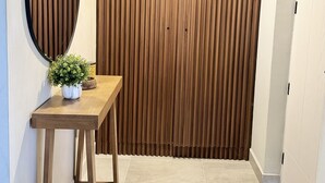 Un couloir avec un mur lambrissé en bois, une table en bois sur laquelle est posée une plante en pot et un sol carrelé.