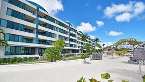 Un hôtel à plusieurs étages doté de balcons, une plage avec des parasols et un panneau indicateur.