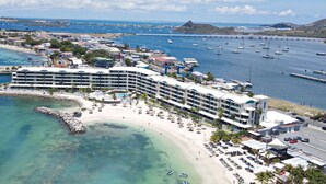 Un hôtel en bord de mer, avec plusieurs étages, une plage et un port de plaisance avec des bateaux.