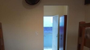 Una habitación con una cama individual, una silla de madera y una puerta que da a un balcón.