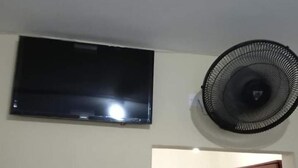 Una habitación con una cama, un televisor montado en la pared y un ventilador de pie.