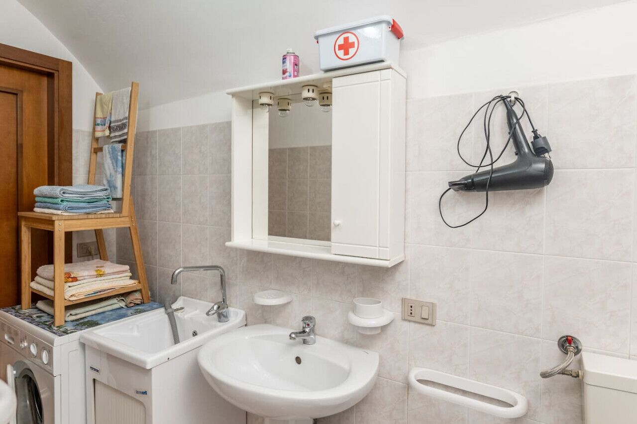 Un baño con lavamanos, espejo, toallero y secador de pelo montado en la pared.